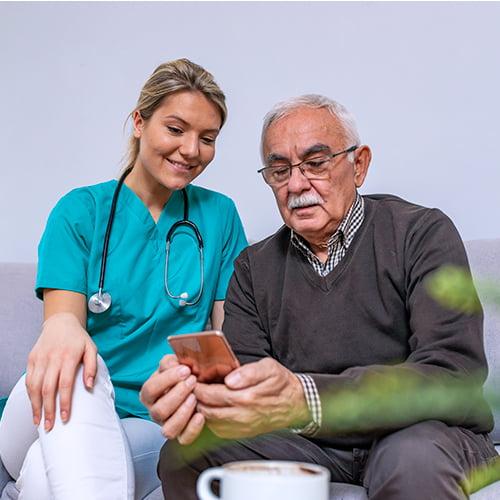 Pflegefachkraft unterstützt älteren Mann bei der Nutzung eines Smartphones.