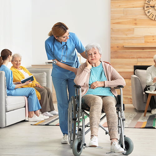 Pflegekraft schiebt eine Seniorin im Rollstuhl im Pflegeheim.